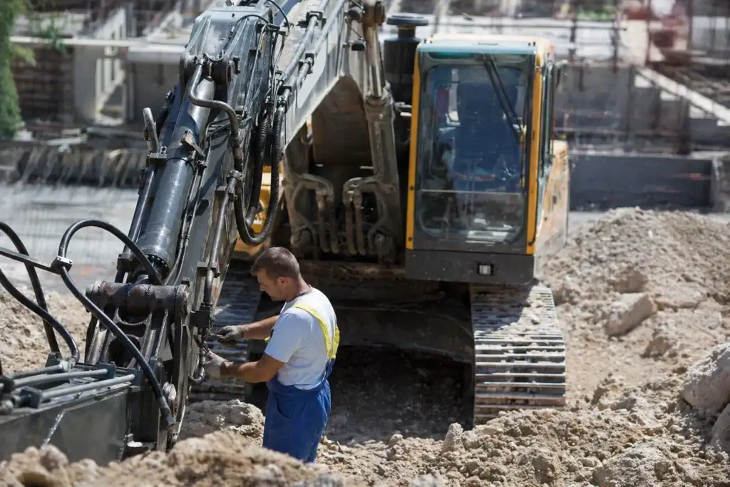 heavy equipment field technician working from service truck with tools and diagnostic laptop repairing excavator on muddy job site