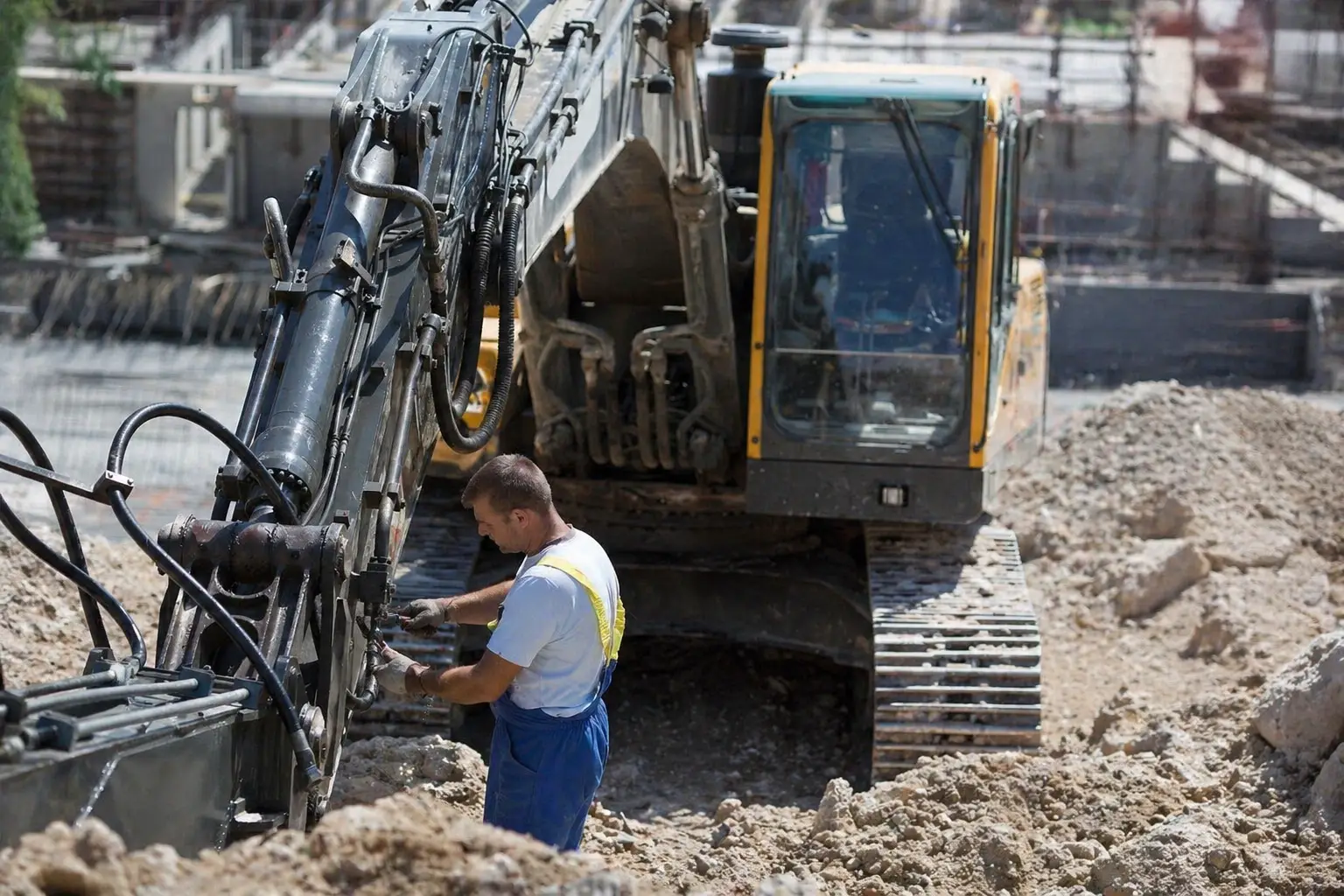heavy equipment field technician working from service truck with tools and diagnostic laptop repairing excavator on muddy job site