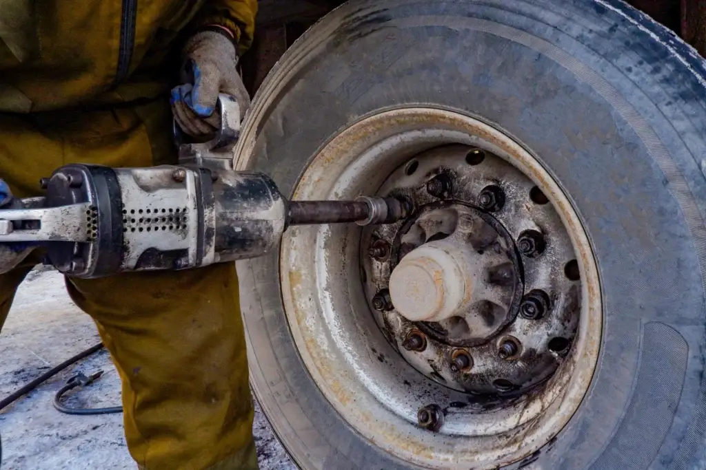 diesel technician using an impact wrench to remove lug nuts from a heavy duty semi truck wheel during tire service