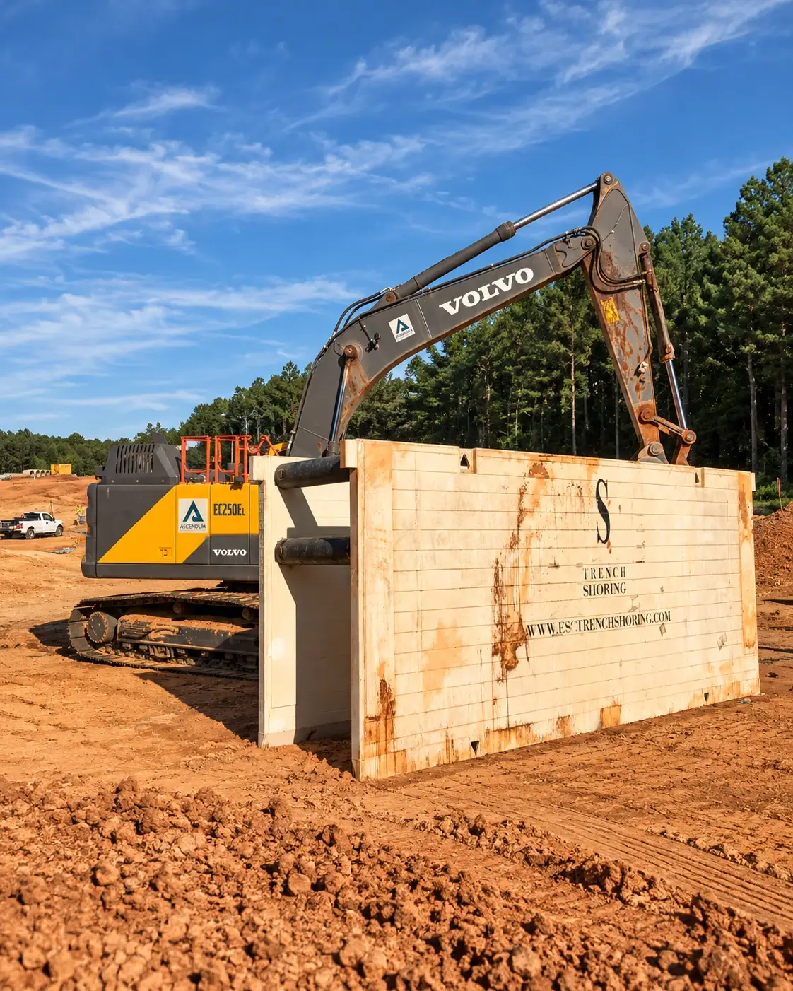Excavator positioned behind a steel trench box at an active construction site, showing heavy-duty trench shoring equipment used for excavation safety.